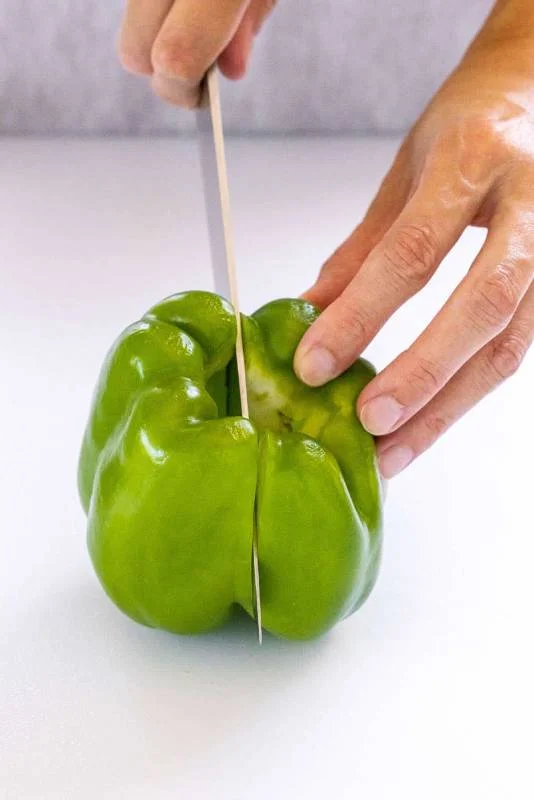Personne tranchant un poivron vert en deux
