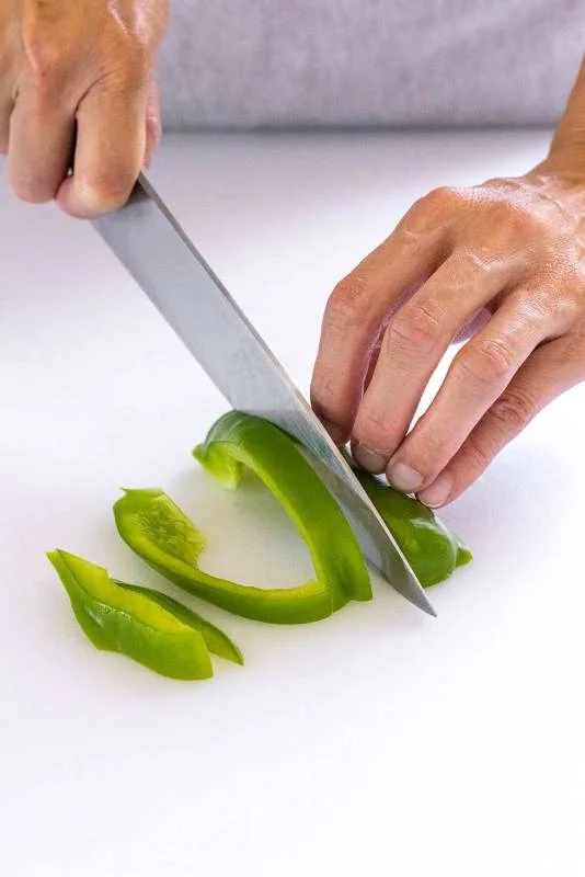 Personne décomposant un poivron vert en lanières