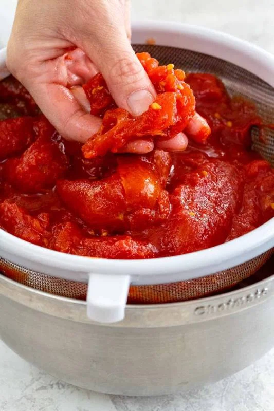 Main écrasant des tomates entières dans une passoire