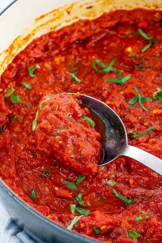 Cuillère en argent mélangeant la sauce marinara dans une grande casserole