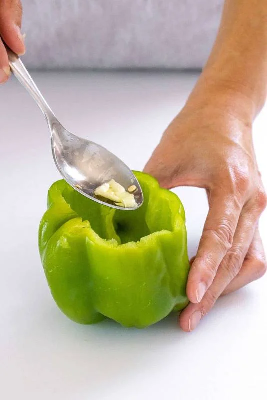Personne utilisant une cuillère pour retirer les graines d'un poivron entier