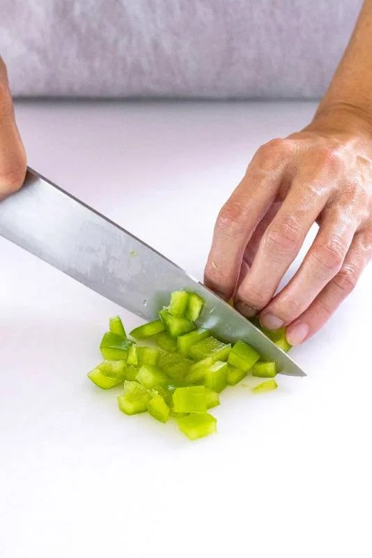 Personne coupant en dés un poivron vert avec un couteau de chef