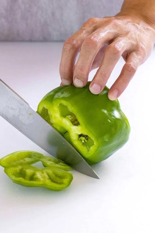 Poivron vert sur une planche à découper blanche avec le dessus et le dessous tranchés