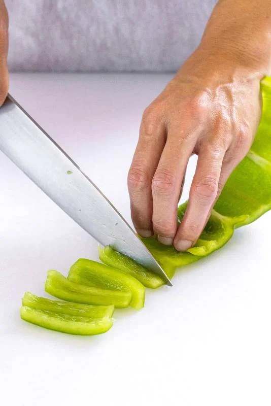 Poivron vert sur une planche à découper blanche étant tranché en petits morceaux