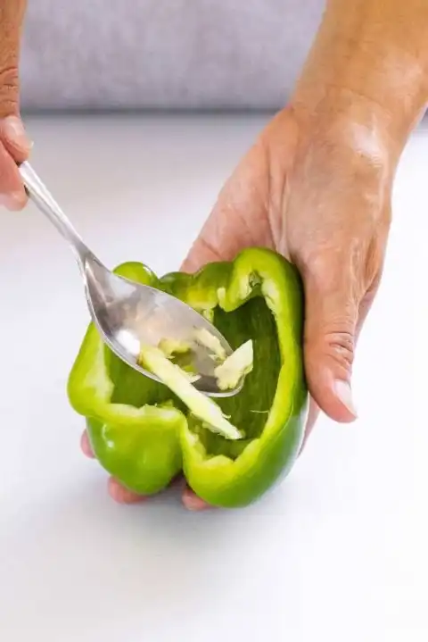 Personne utilisant une cuillère pour retirer la membrane d'une moitié de poivron