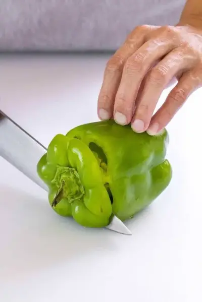 Personne coupant le dessus d'un poivron vert avec un couteau de chef