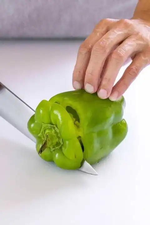 Personne coupant le dessus d'un poivron vert avec un couteau de chef