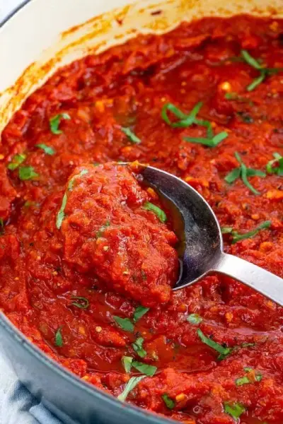 Cuillère en argent mélangeant la sauce marinara dans une grande casserole
