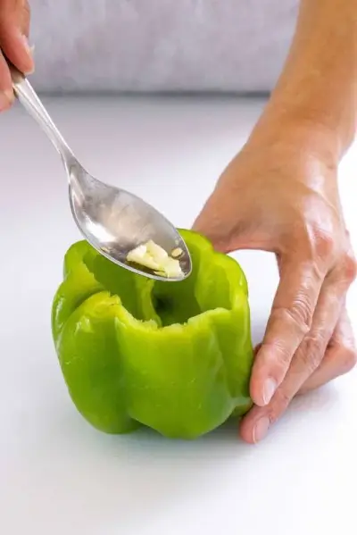 Personne utilisant une cuillère pour retirer les graines d'un poivron entier