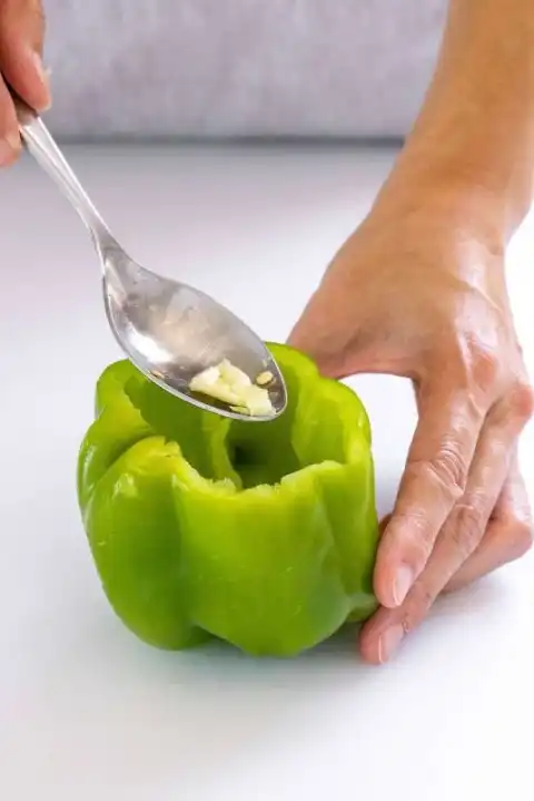 Personne utilisant une cuillère pour retirer les graines d'un poivron entier
